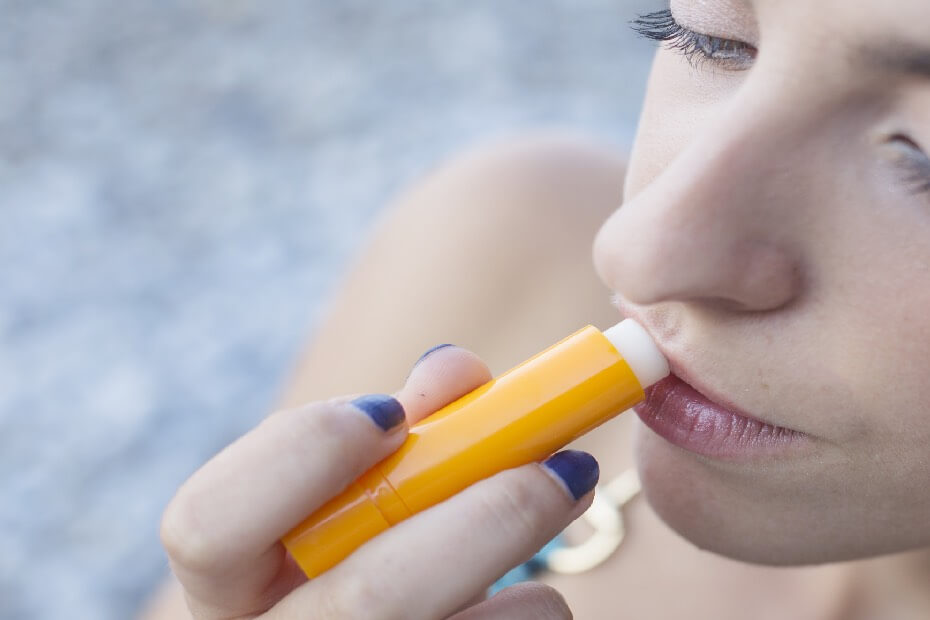 Mujer en la playa hidratándose los labios, sobre tips de maquillaje para lucir radiante en la playa