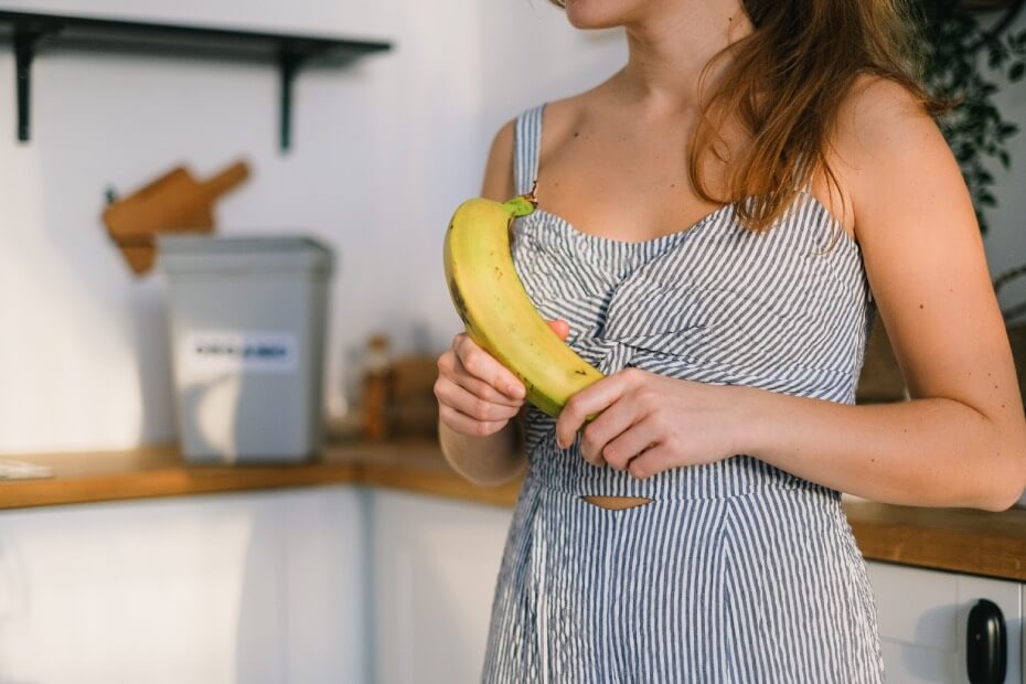 Mujer sosteniendo un plátano que contiene biotina, la cual es esencial para la salud de la piel
