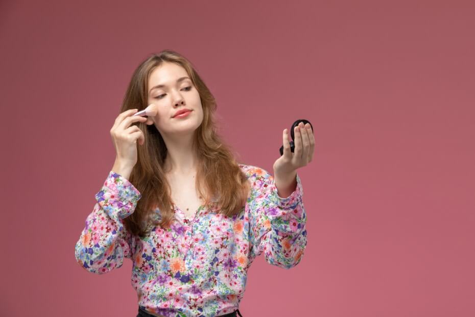 Una mujer de frente maquillándose y sujetando un espejo de mano, sobre las 6 mejores marcas de maquillaje cruelty free para una belleza consciente