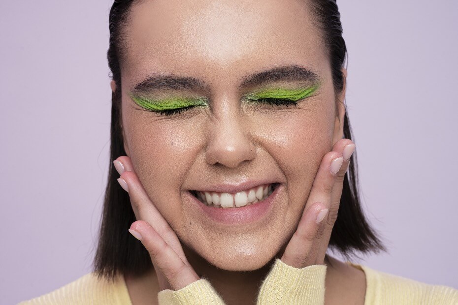 Mujer de frente sonriendo con sobras verdes en los ojos y sujetándose el rostro