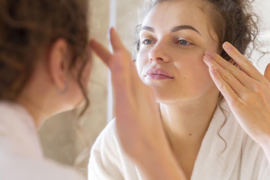 Mujer frente a un espejo observando su tipo de piel para un maquillaje ideal