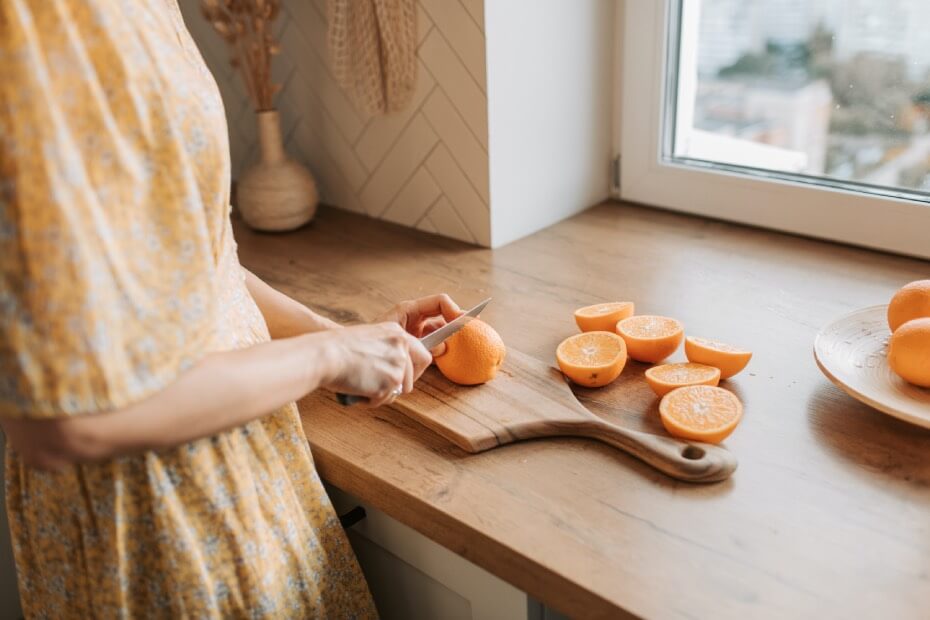 Mujer cortando naranjas que contienen vitamina C, una vitamina antioxidante recomendada para lucir una piel radiante