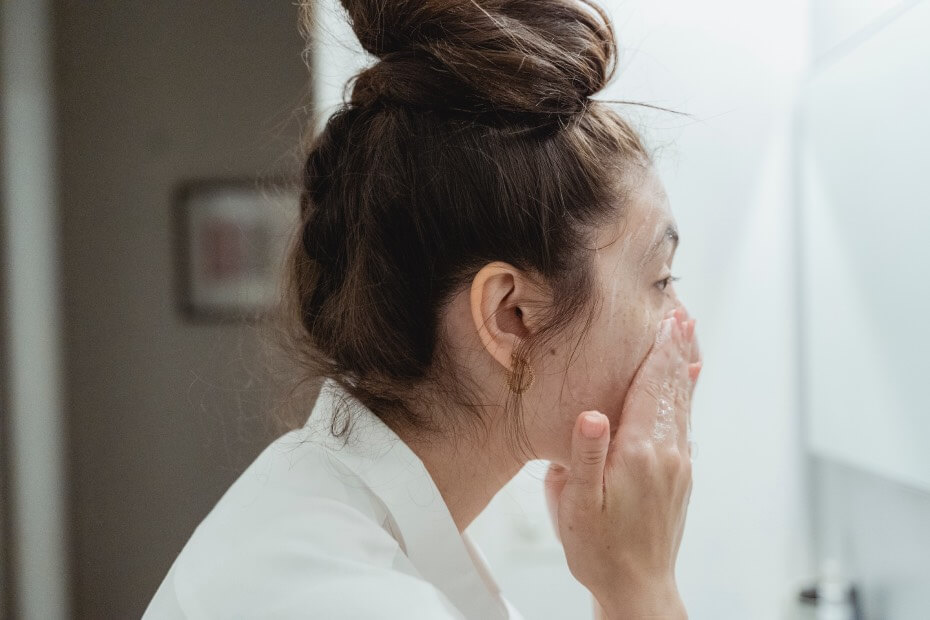 Novia limpiando su piel frente al espejo, para tener la piel limpia para el maquillaje el día de su boda