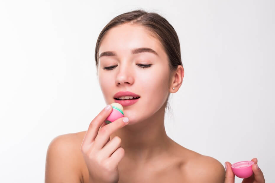 Mujer de frente sosteniendo y aplicándose un labial para proteger sus labios del frío