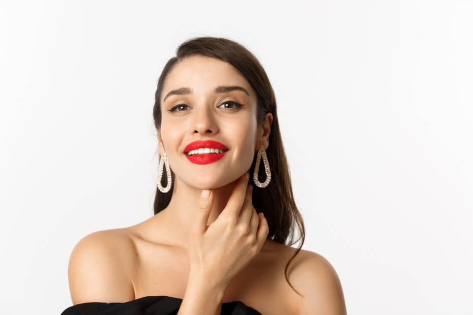 Hermosa mujer morena con labios rojos tocandose la cara y sonriendo