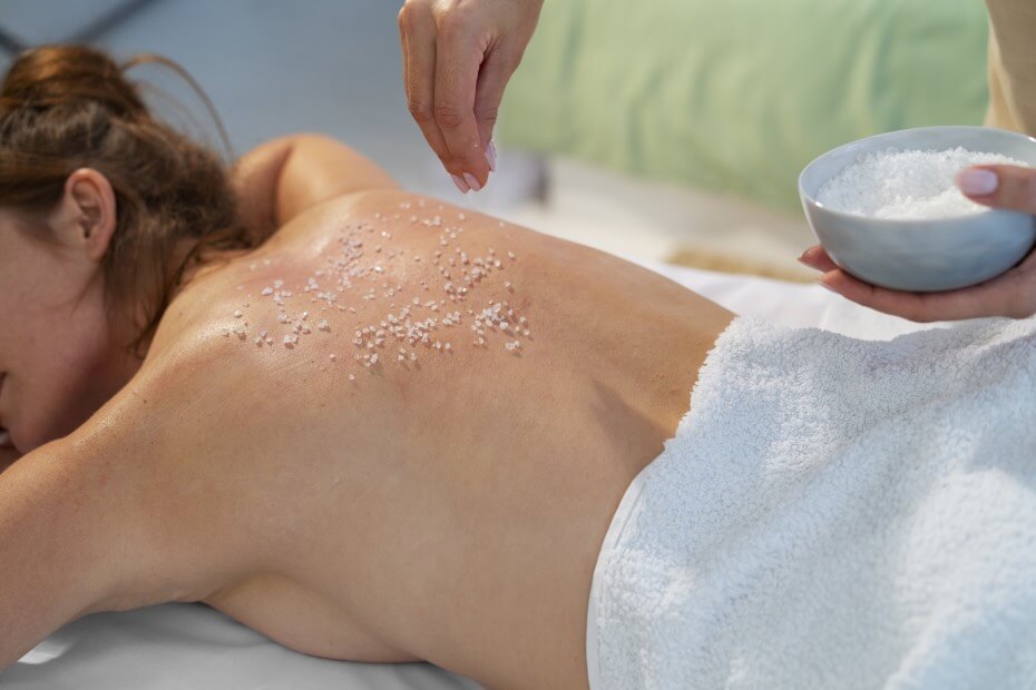 Mujer en un spa acostada boca abajo recibiendo una exfoliación profunda en el cuerpo