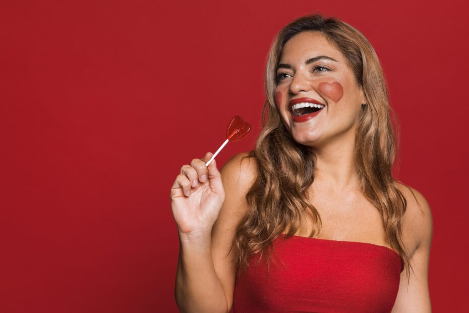 Mujer sonriente posando con labial rojo de Mac en fondo rojo como recomendación de Foriu para San Valentin
