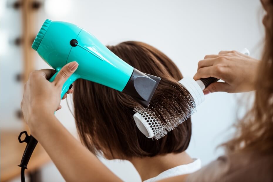Estilista aplicando protección térmica en cabello antes de secarlo